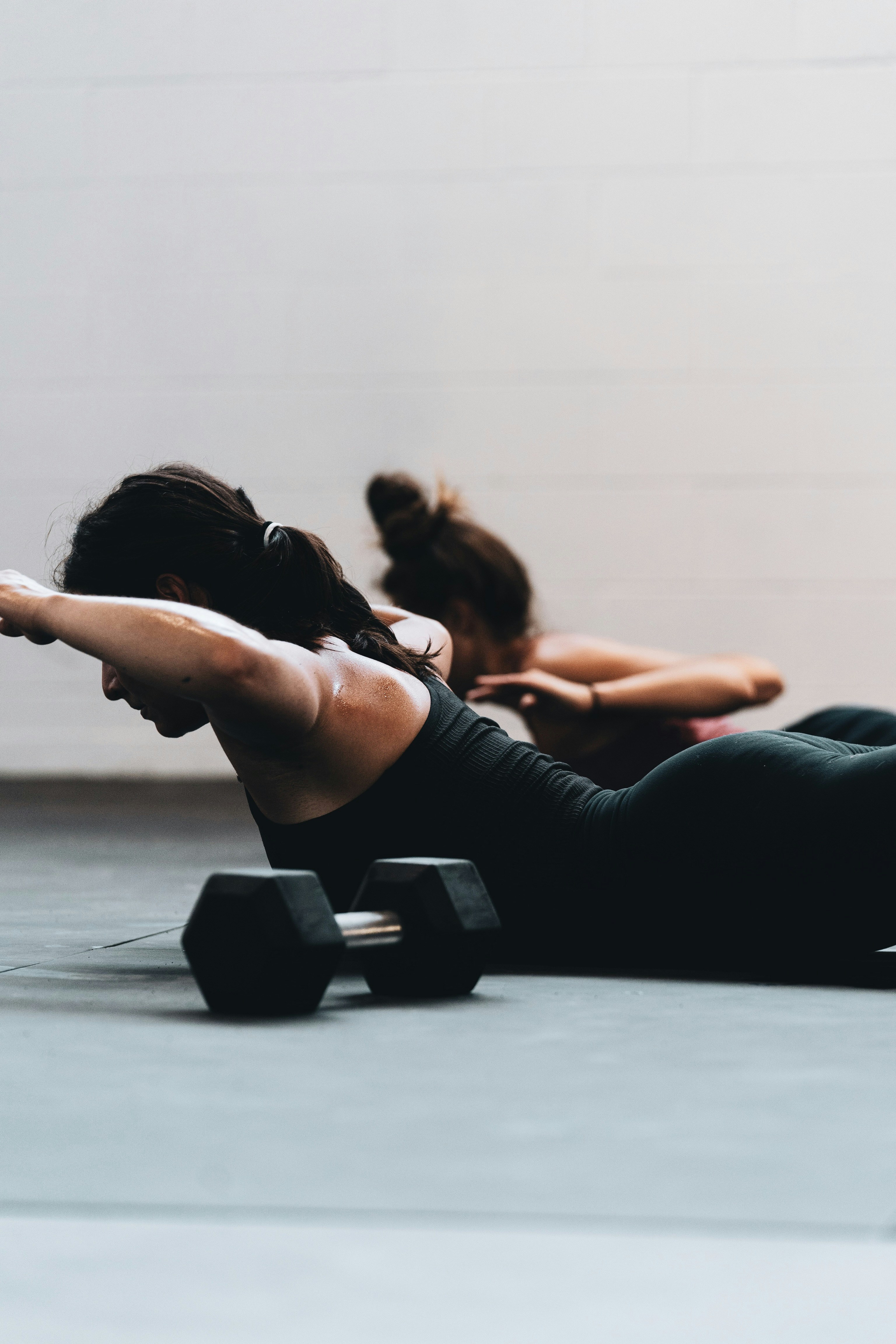 Two women in matching low extensions on a studio floor.